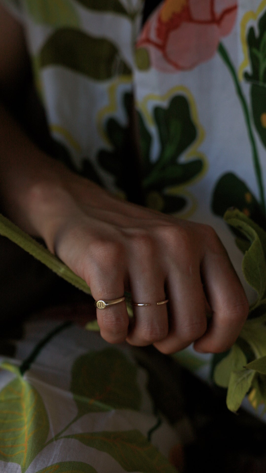 Close-up of a hand wearing solid gold rings with a floral-patterned background