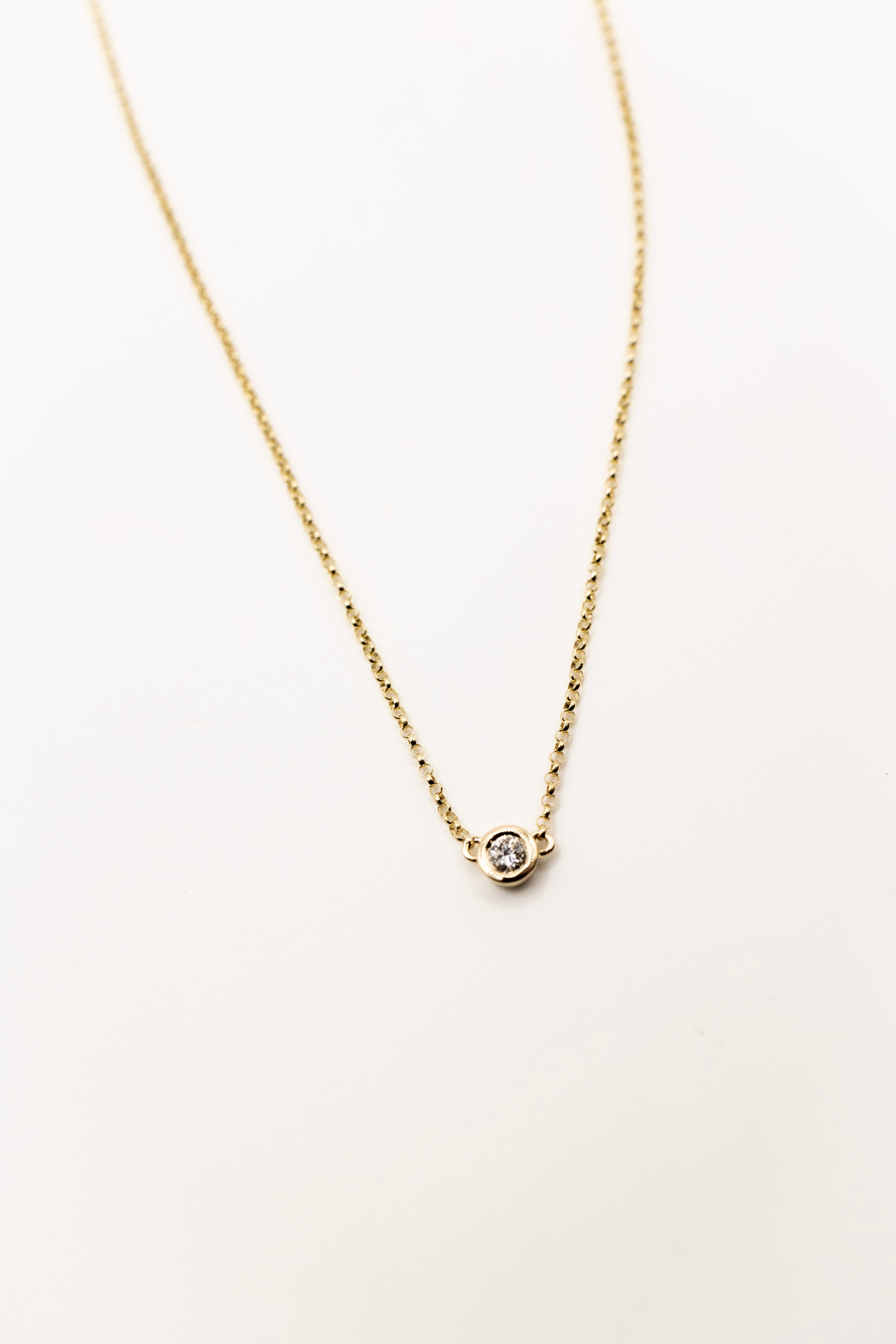 Gold necklace with a small diamond pendant on a light beige background