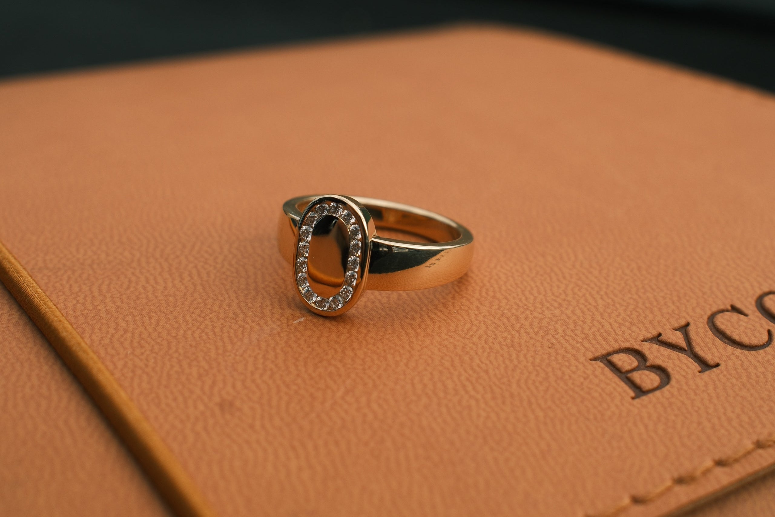 Close-up of a gold ring with a diamonds on a brown leather surface.
