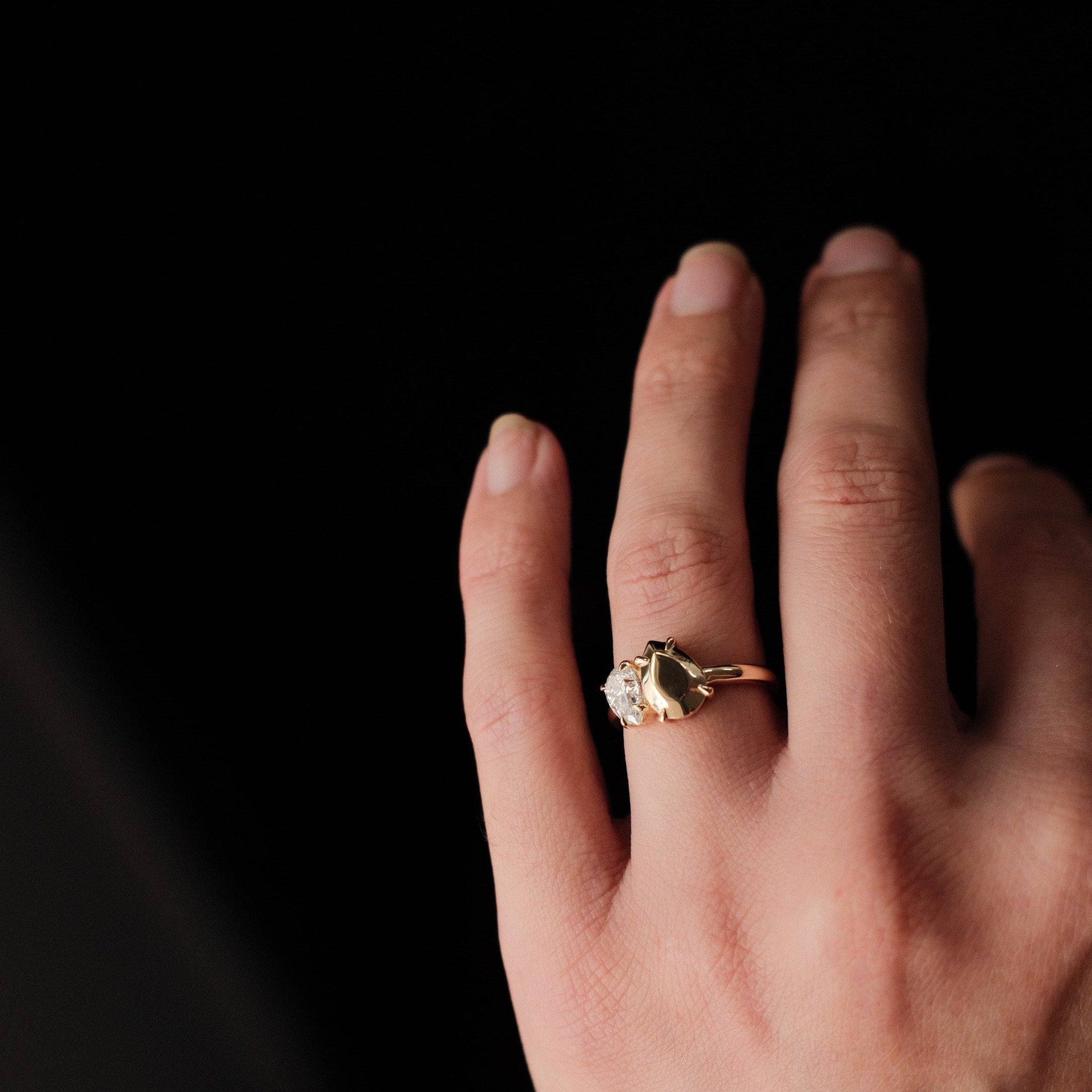 Hand wearing a gold ring with a diamond on a black background