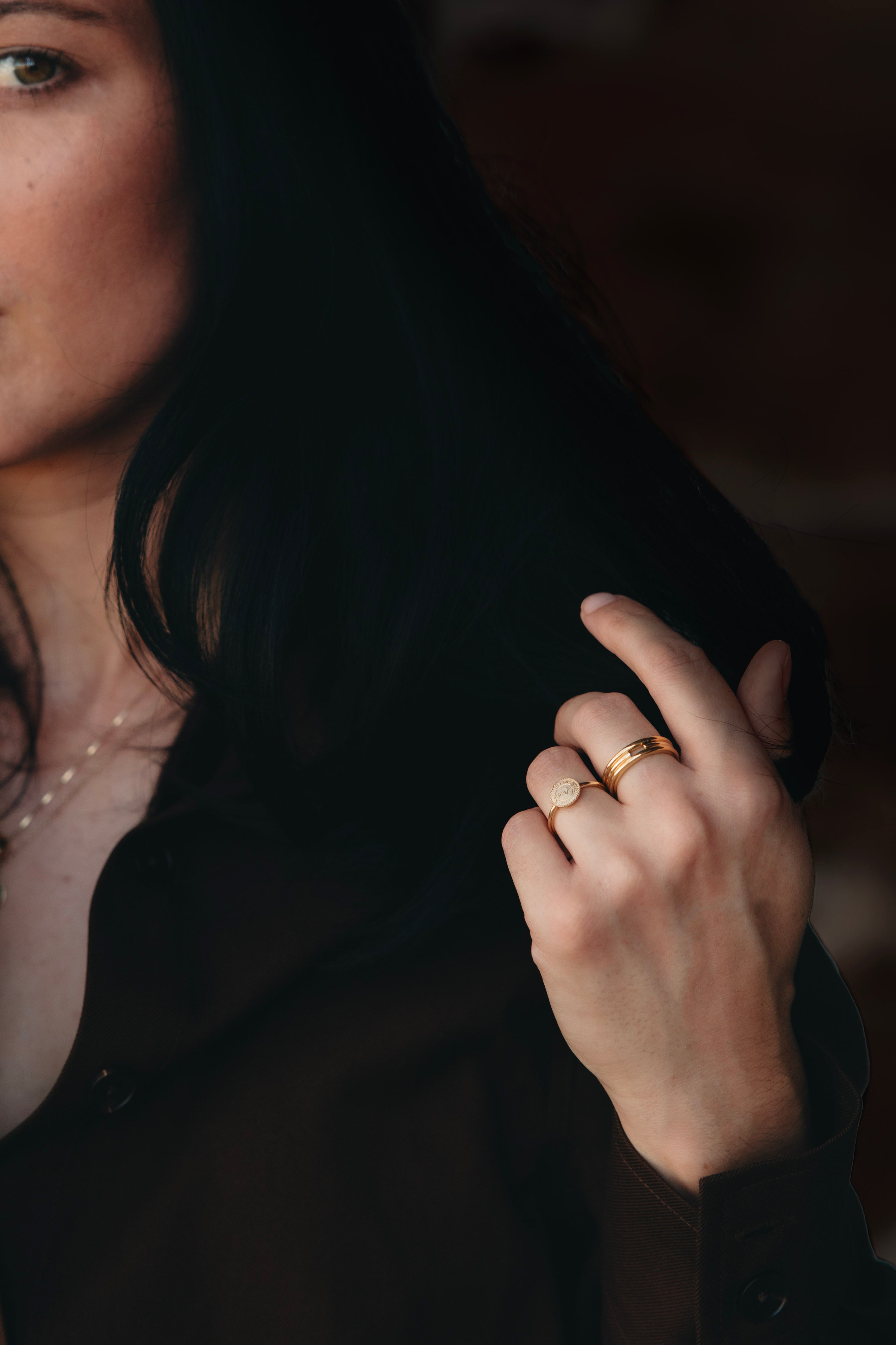 Solid gold signet ring worn alongside plain gold bands in a simple ring stack