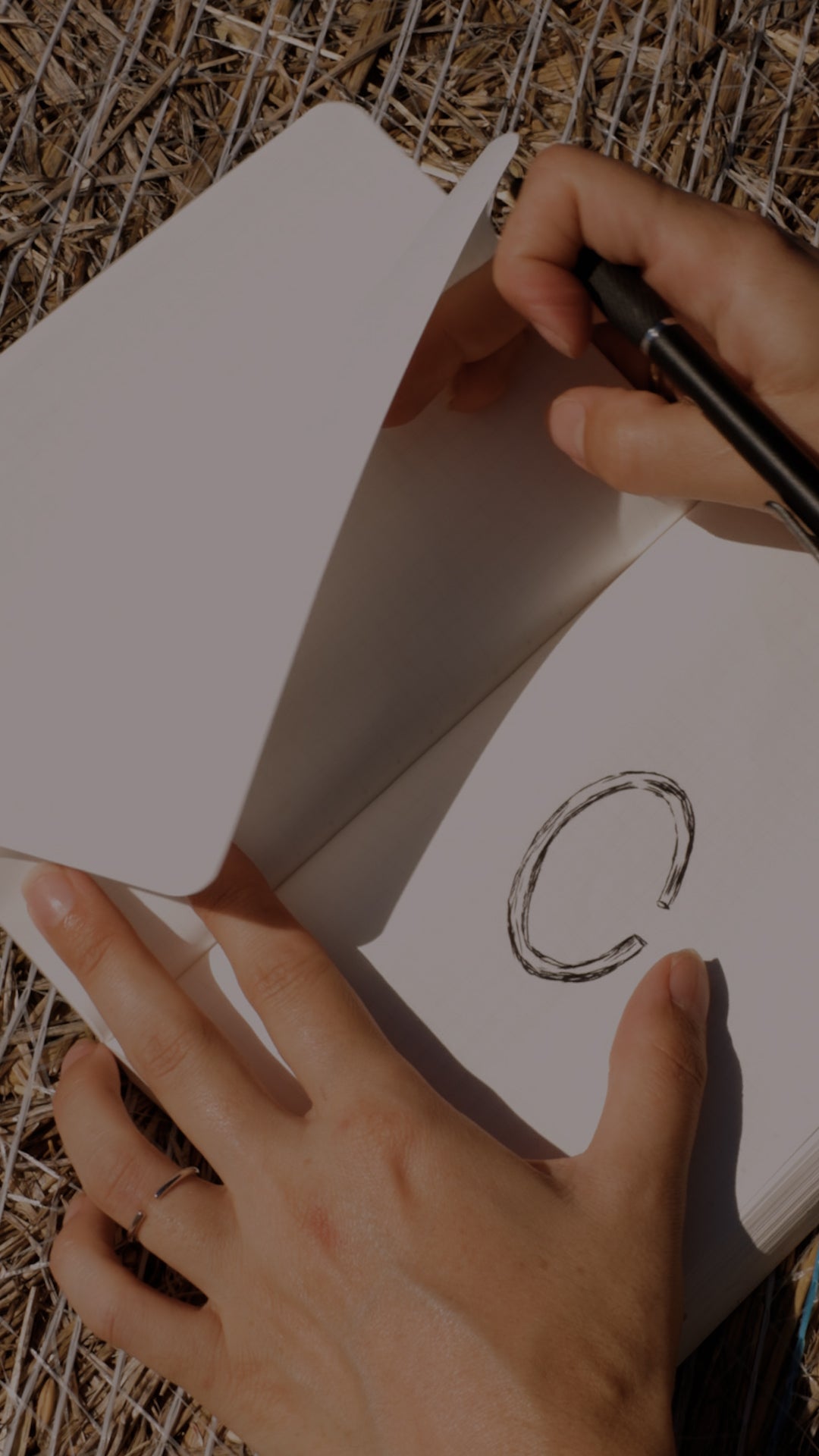 Person designing open ended ring piece of paper with a pen outdoors.