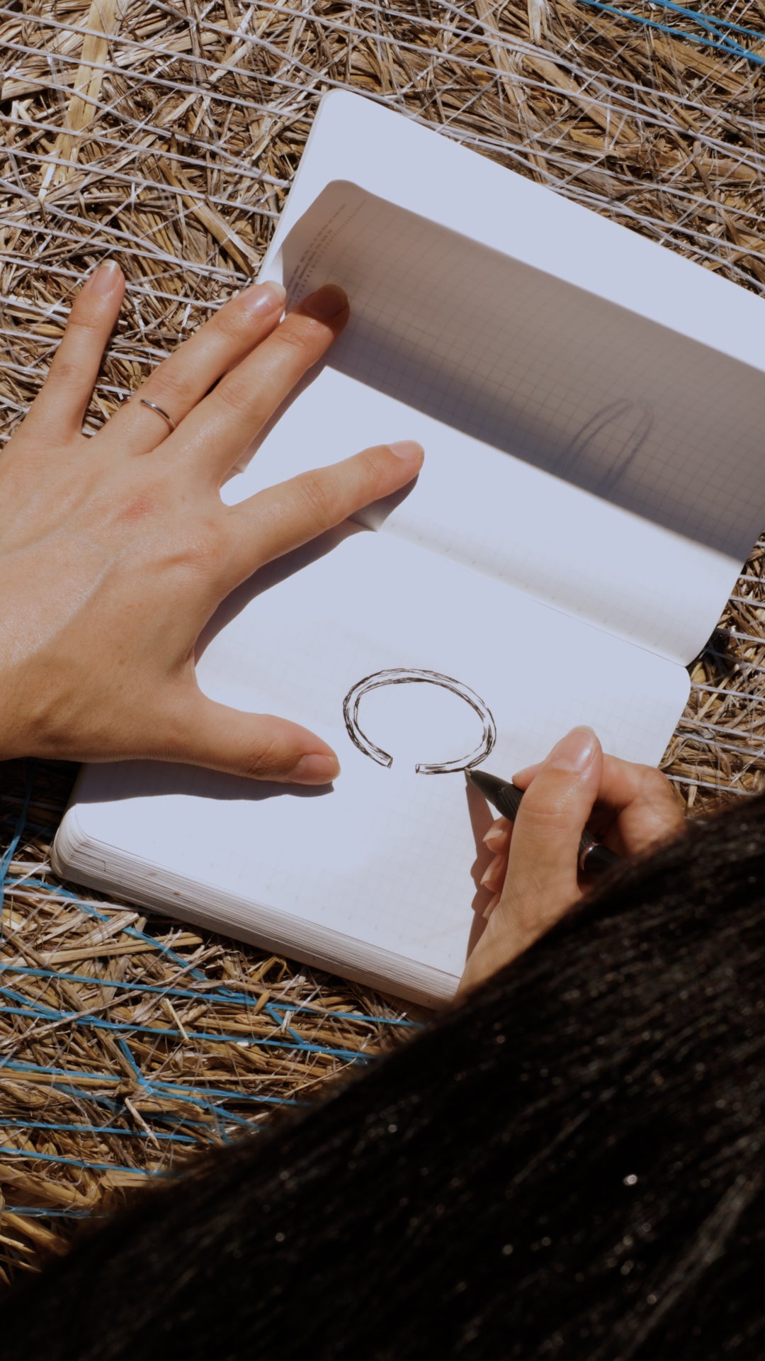 Person drawing ring design in a notebook on a straw background. Australian gold, NSW design