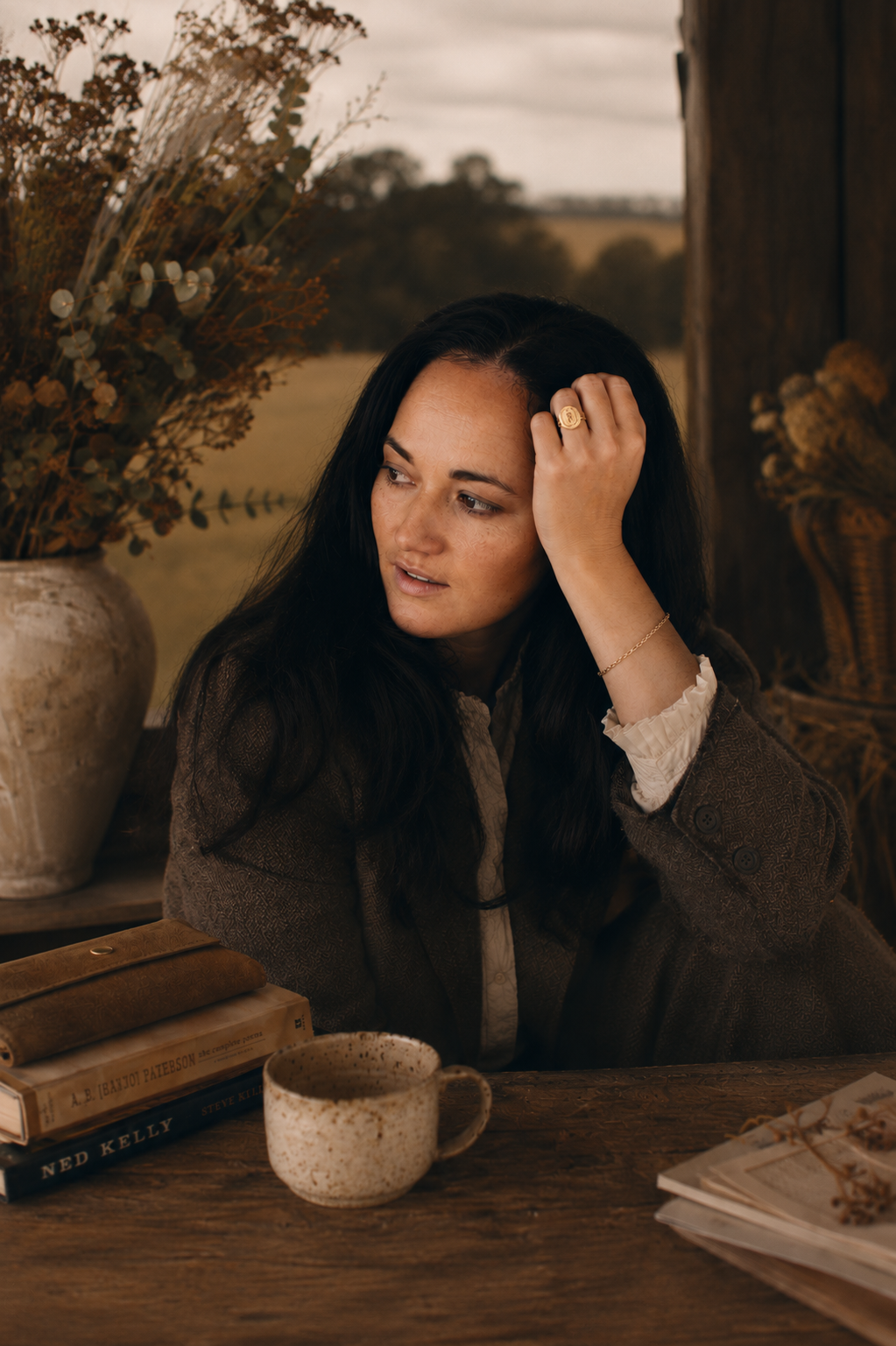 Woman sitting at a table with a cup and books, surrounded by decorative elements.